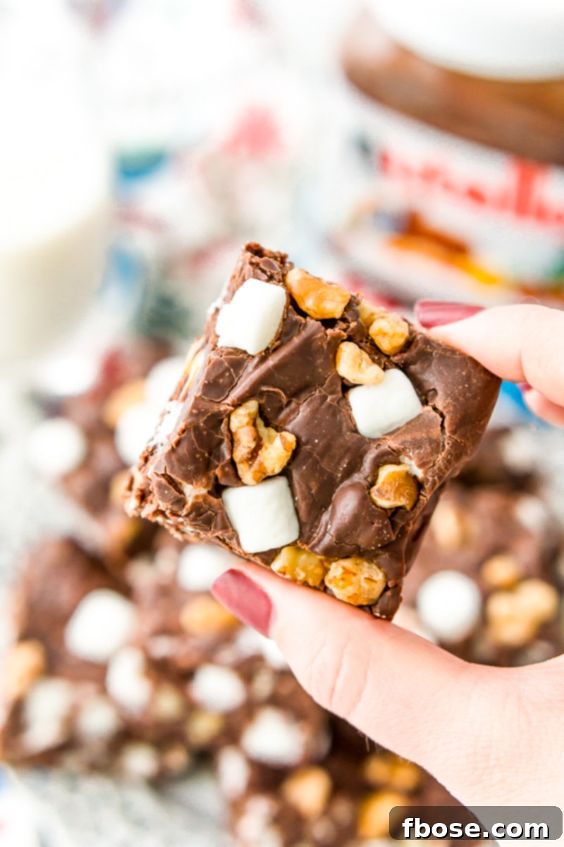 Various squares of Nutella Rocky Road Fudge on a festive white plate, loaded with marshmallows, walnuts, and chocolate chips, ready to be enjoyed as an easy and delicious treat.