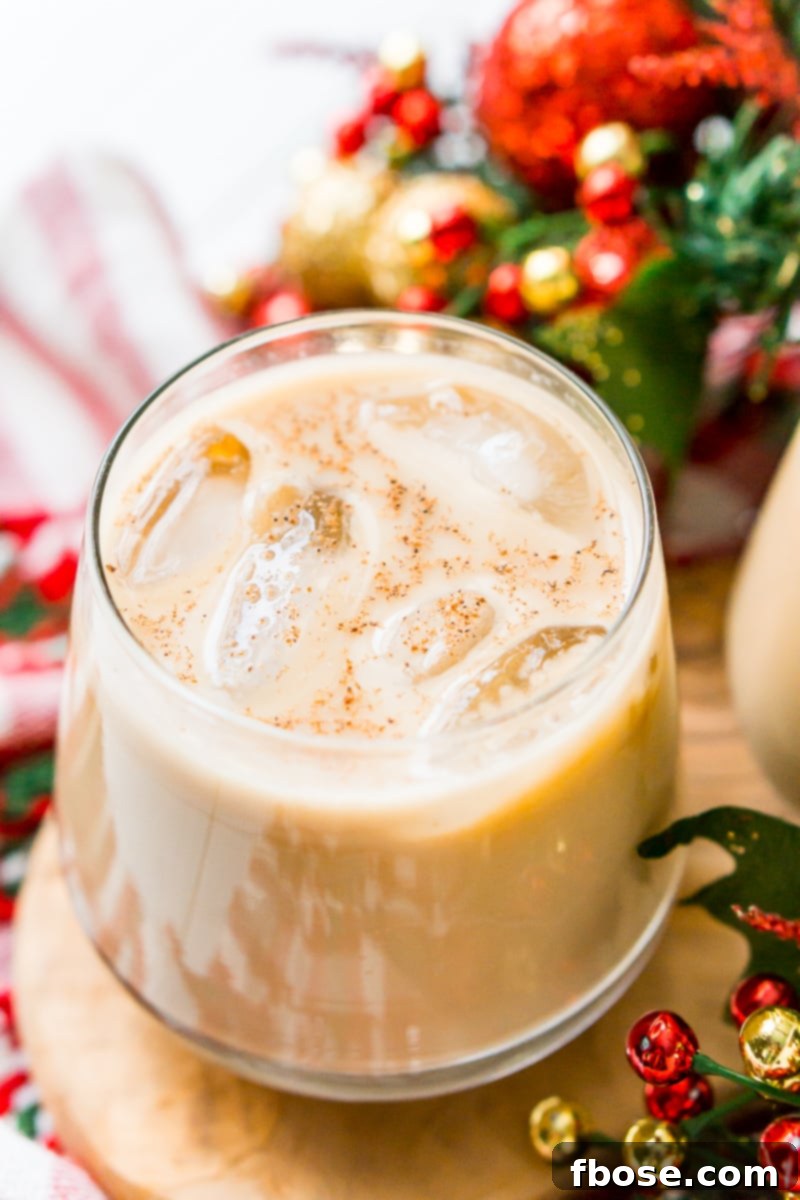 A beautifully garnished Eggnog White Russian cocktail in a short rocks glass, with a cinnamon stick and fresh nutmeg.