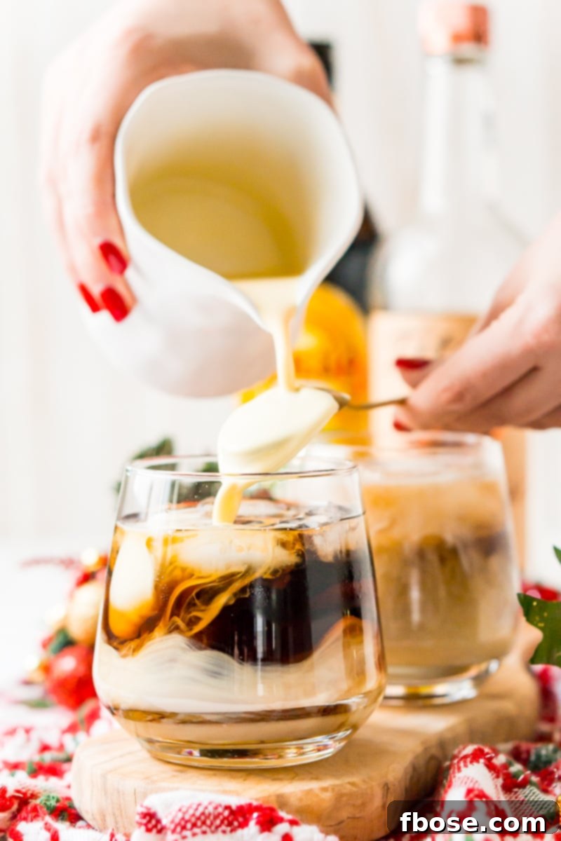 An Eggnog White Russian cocktail being poured, showing the layering effect of eggnog over the dark coffee liqueur and vodka.