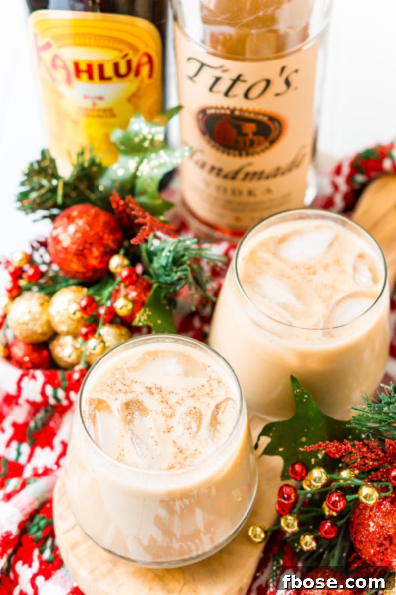 Four festive Eggnog White Russians on a wooden tray, garnished with straws, cinnamon sticks, and maraschino cherries.