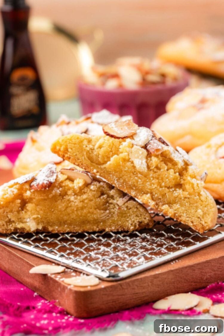 Almond croissant cookies on a serving board, one has been sliced in half to show the frangipane filling.