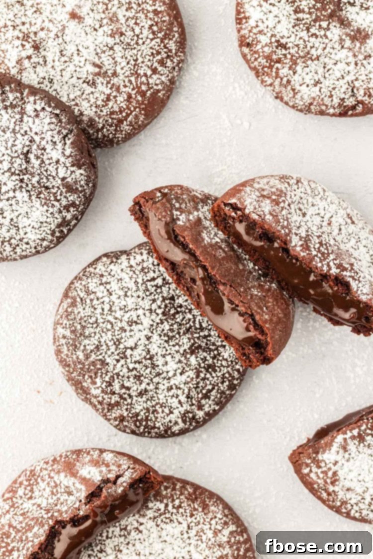 Overhead photo of molten lava cake cookies on a white table, some broken in half to reveal the gooey center.