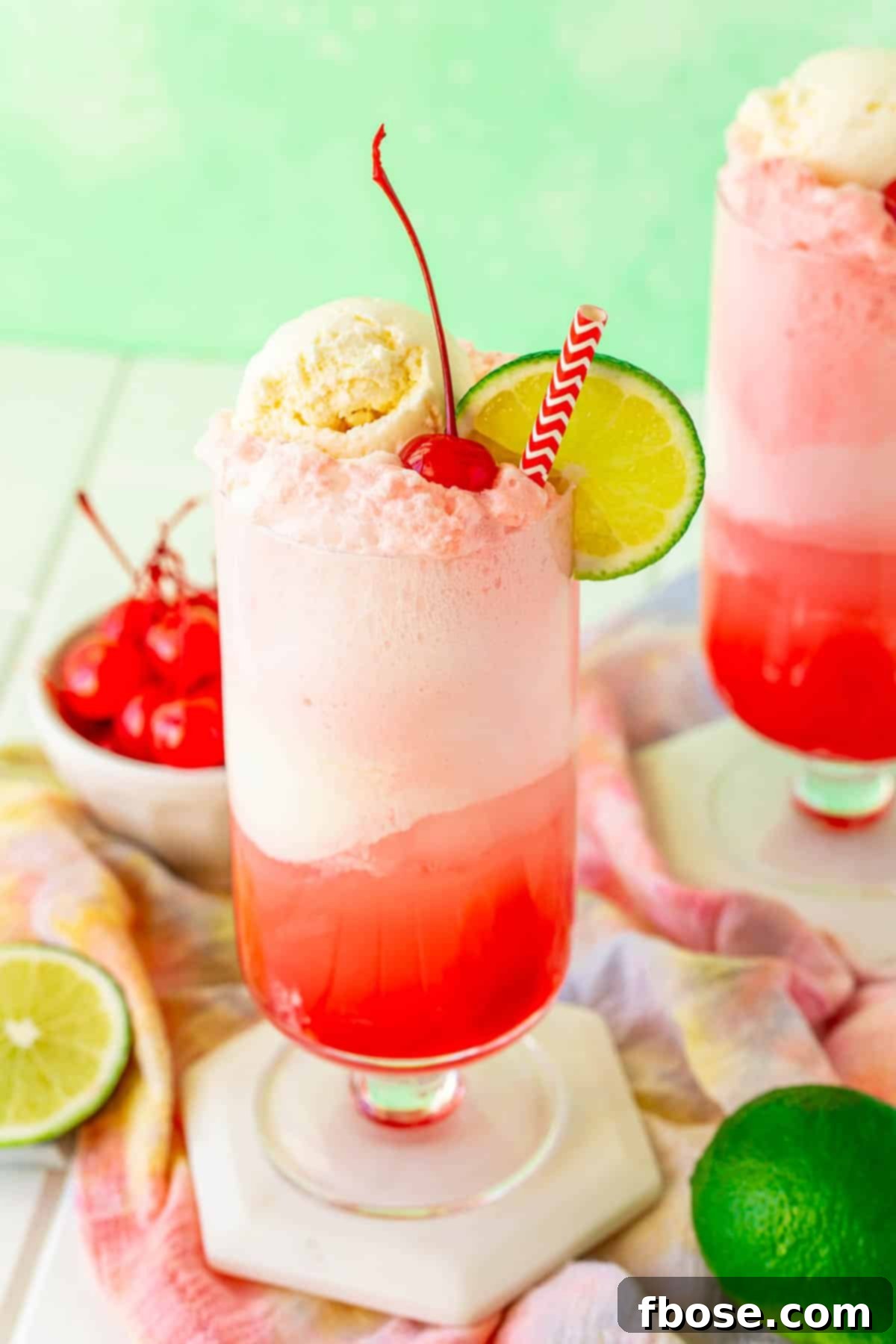 Shirley Temple float on a white coaster with limes and maraschino cherries around it.