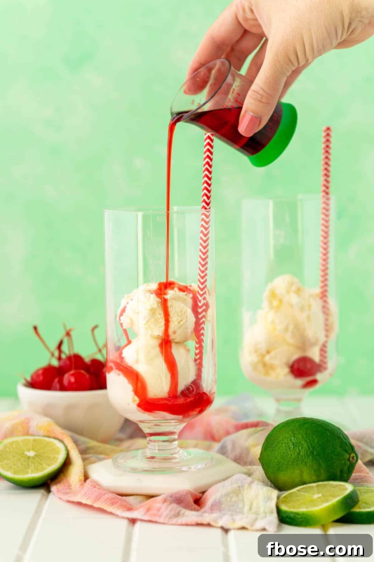 Grenadine syrup being poured over scoops of vanilla ice cream in a glass.