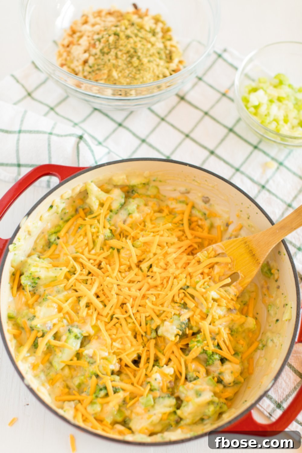 Pot with fresh ingredients for Broccoli Cheese Casserole being mixed with a spoon, showing vibrant broccoli, onions, and cheese.