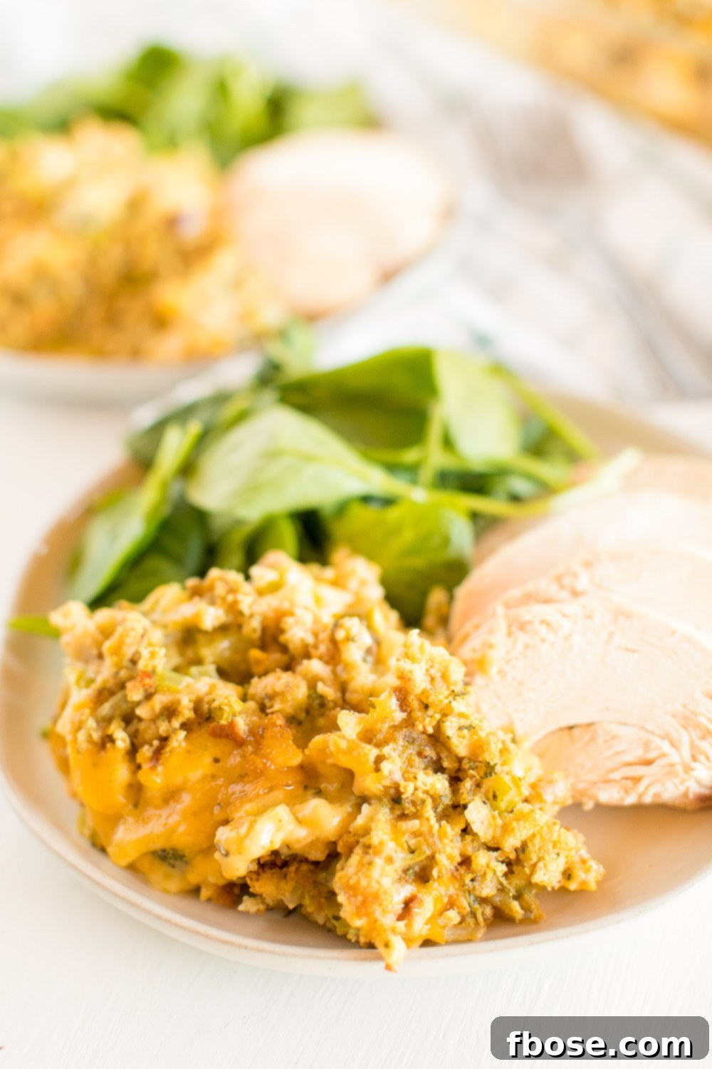 Plate with a generous serving of Broccoli Cheese Casserole, alongside a grilled chicken breast and a fresh green salad.