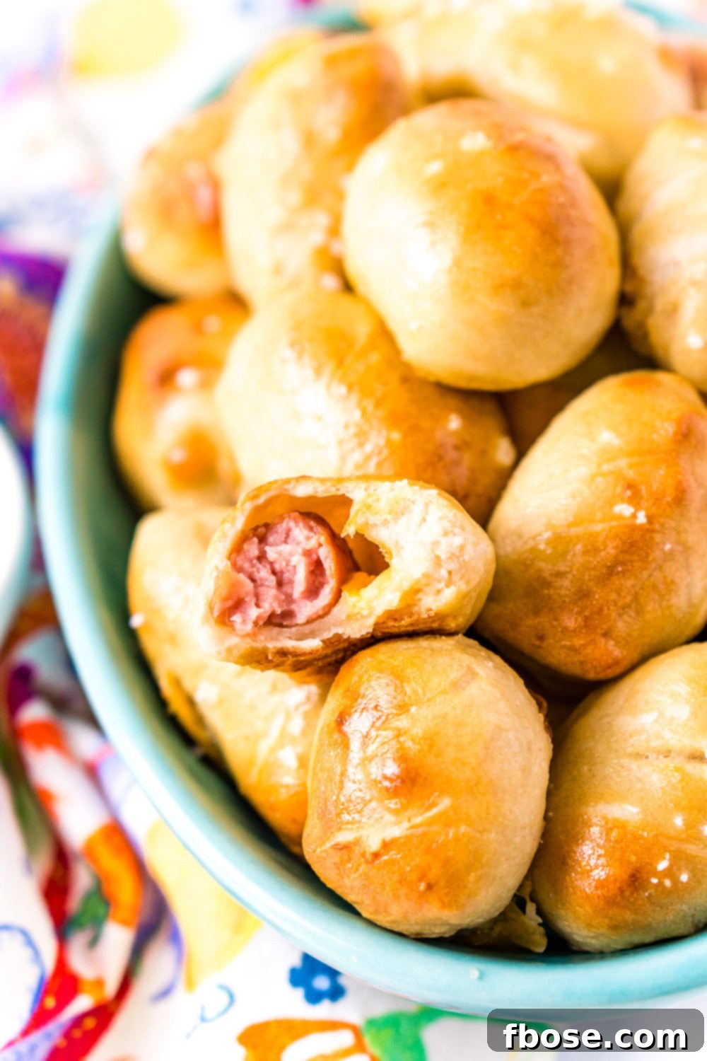 Bowl of pretzel pigs in a blanket with bite taken out of one.