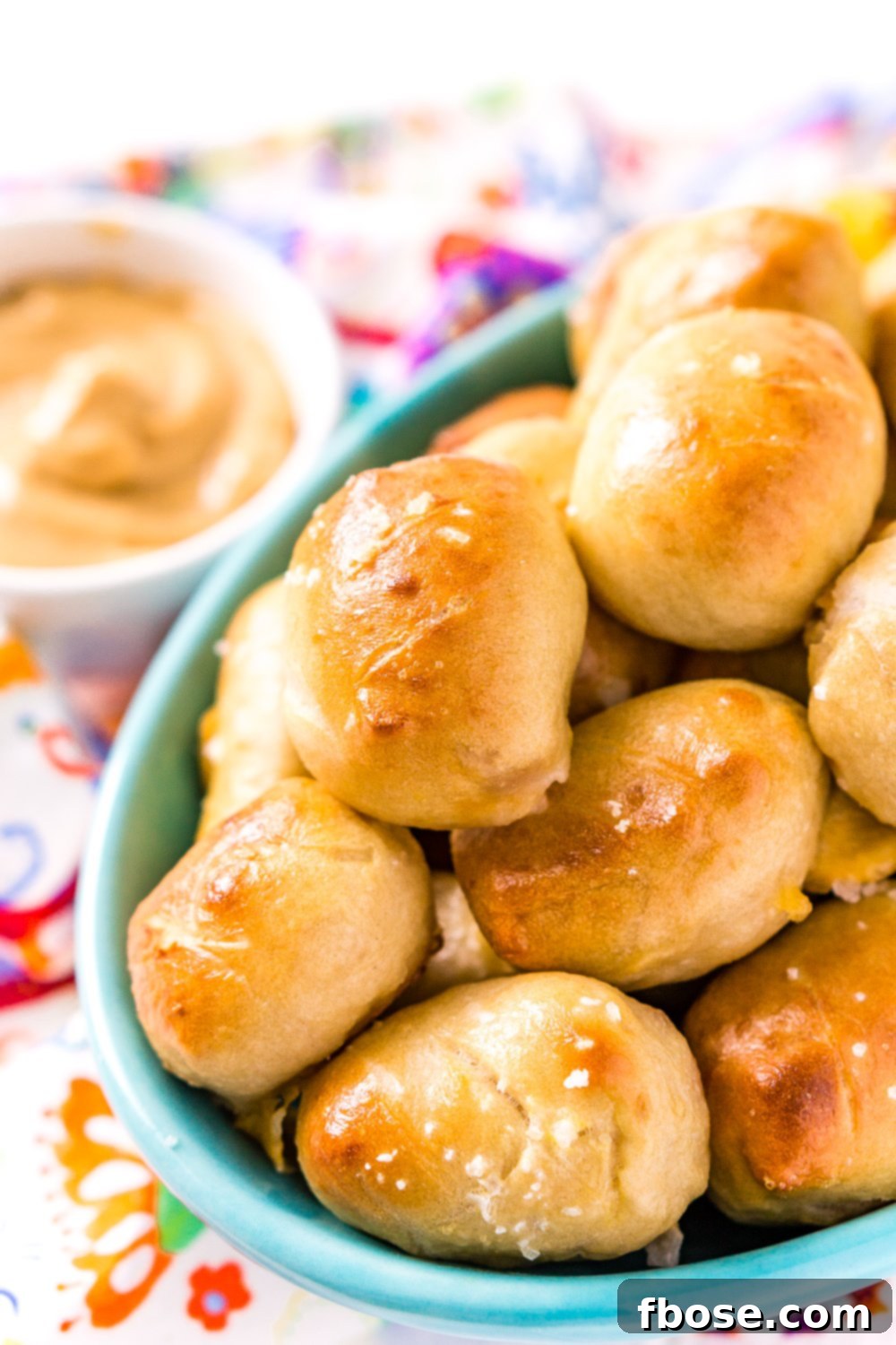 Pretzel Pigs In A Blanket in a teal bowl with dipping sauce in the background.