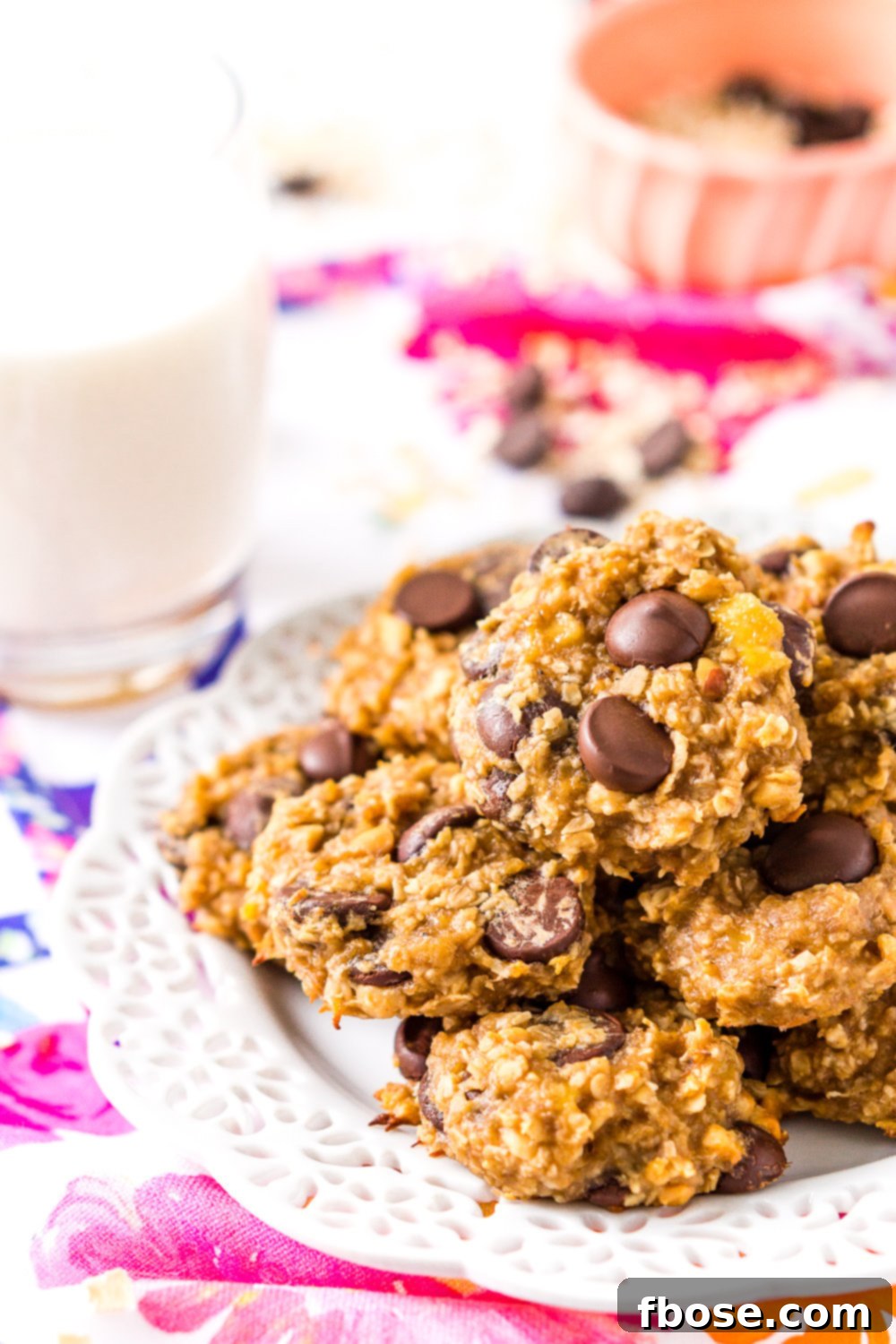 Banana Oatmeal Cookies on white plate on colorful napkin with glass of milk and pink bowl in background