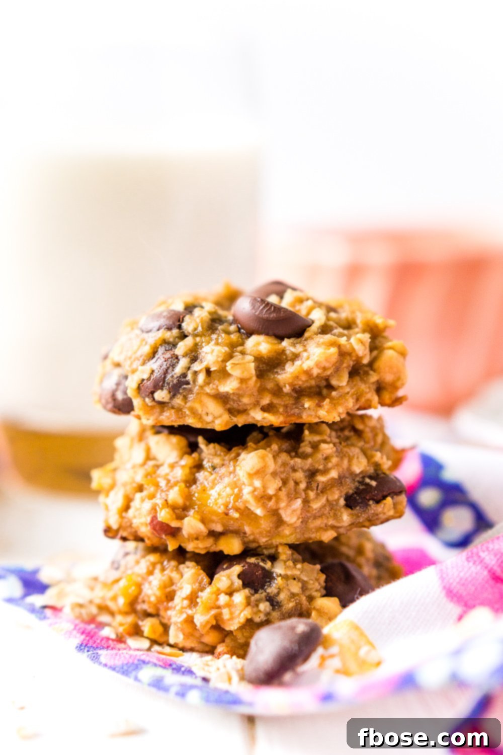Banana Oatmeal Cookies with chocolate chip stacked three high with milk in background.