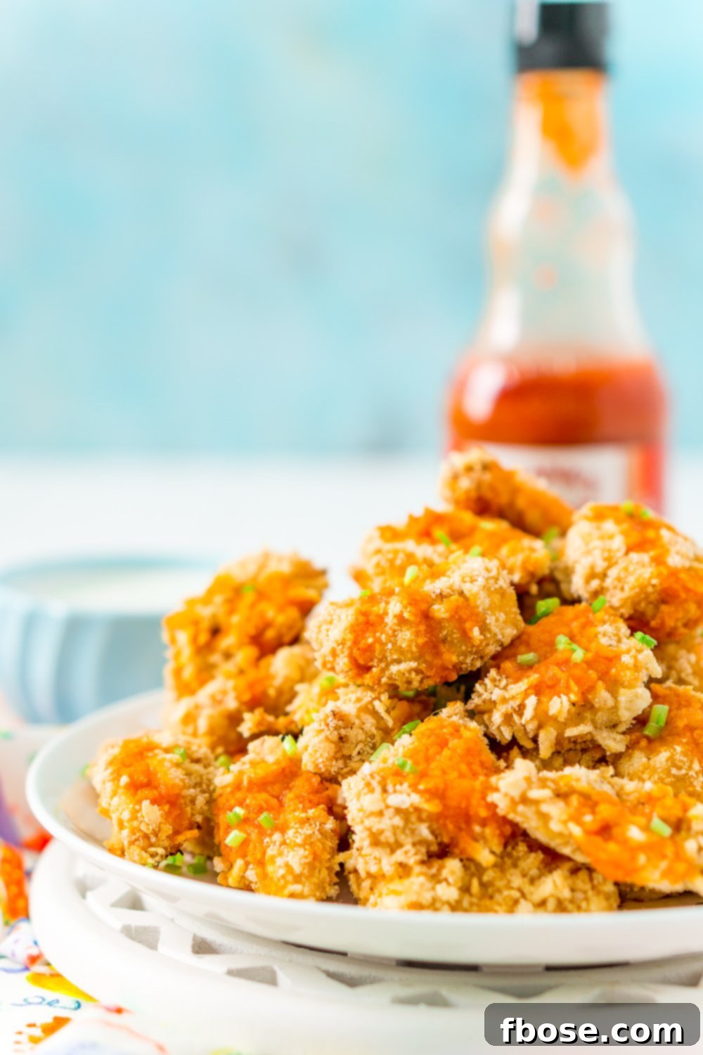 Plate of crispy baked chicken wings with hot sauce bottle in background and blue wall background.