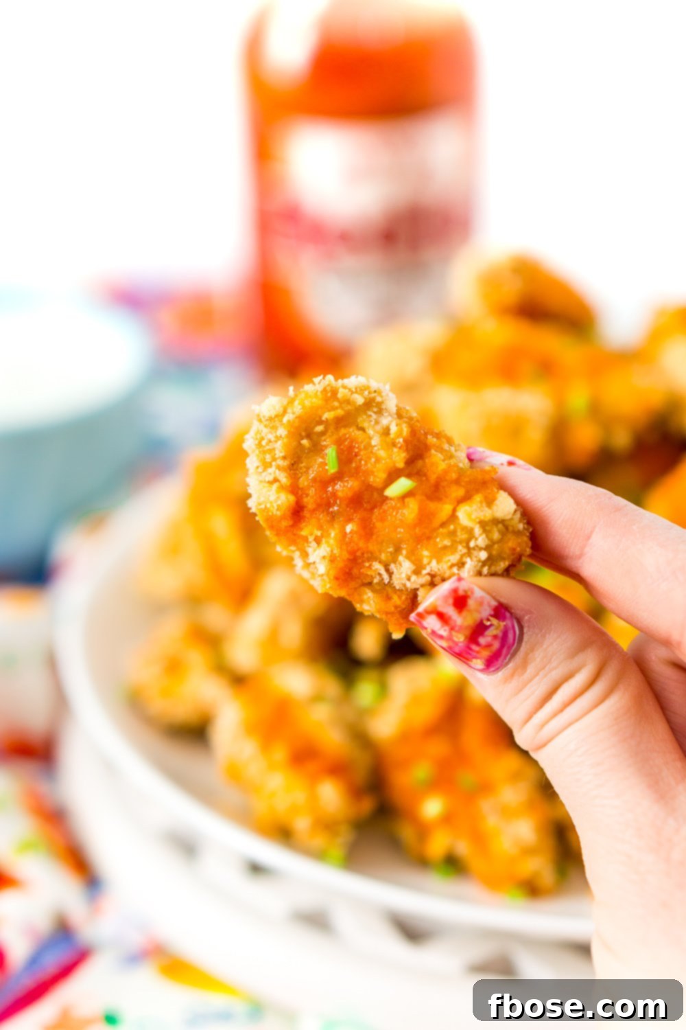 Woman's fingers holding Crispy Baked Chicken wing with buffalo sauce.