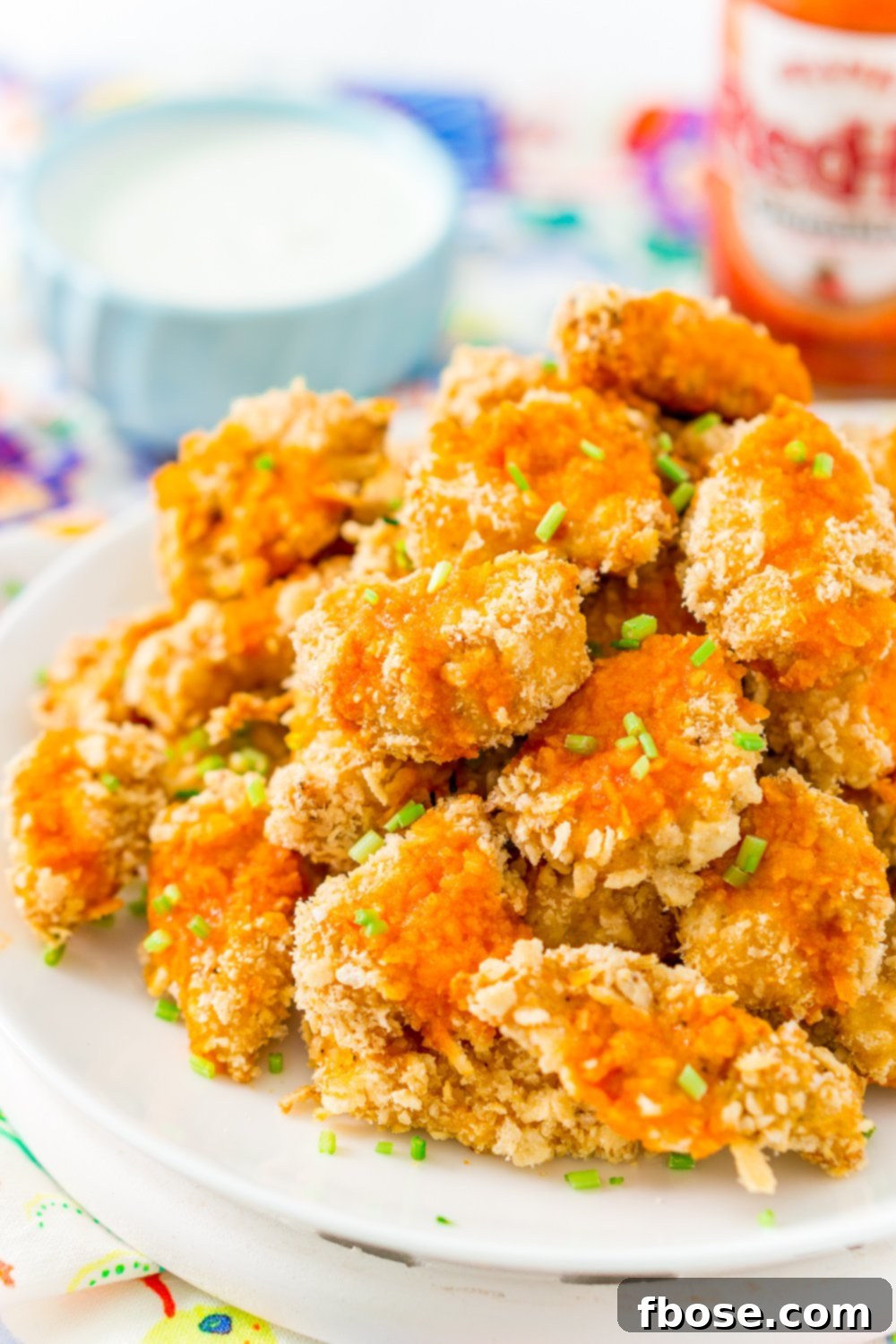 Crispy Baked Chicken Wings on a white plate with dipping sauce and hot sauce bottle in the background.