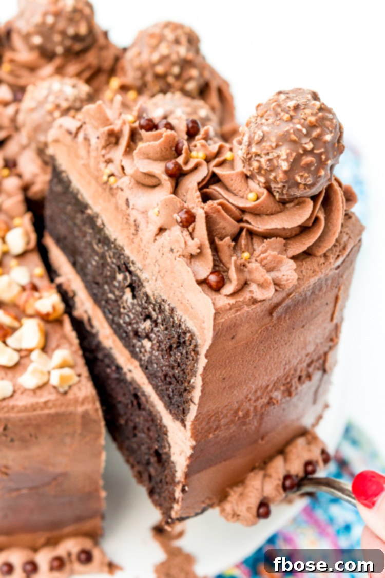 A hand gently lifting a slice of frosted Nutella cake from a larger cake on a white cake stand, revealing its moist layers.