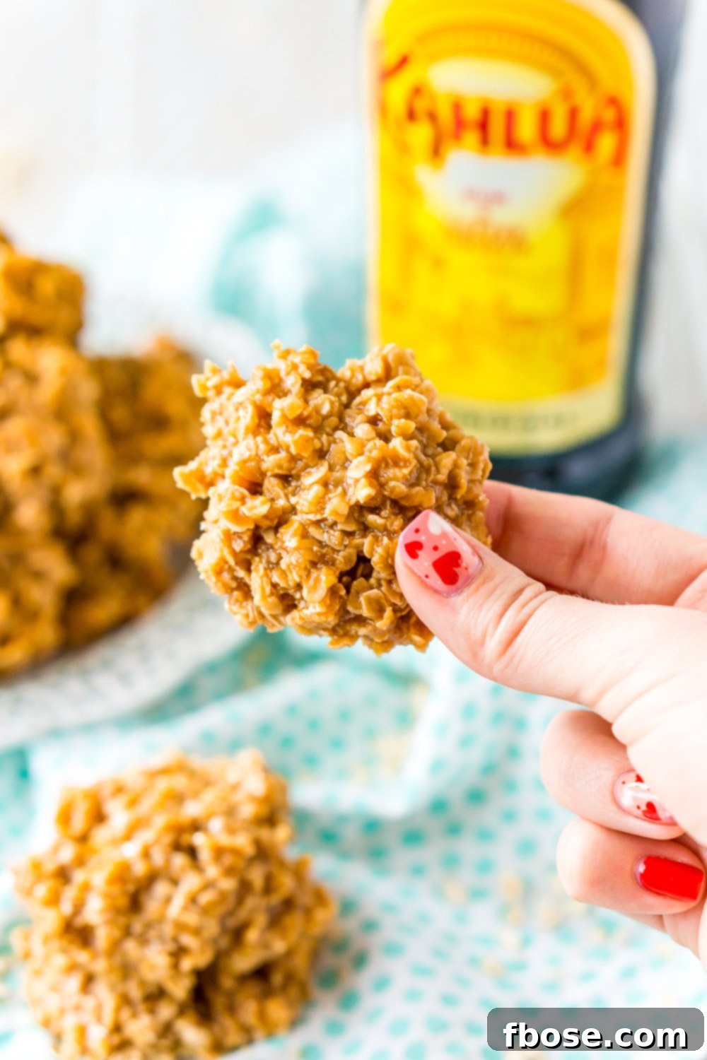 Woman's hand holding a Kahlua No Bake Cookie with bottle of Kahlua in the background.