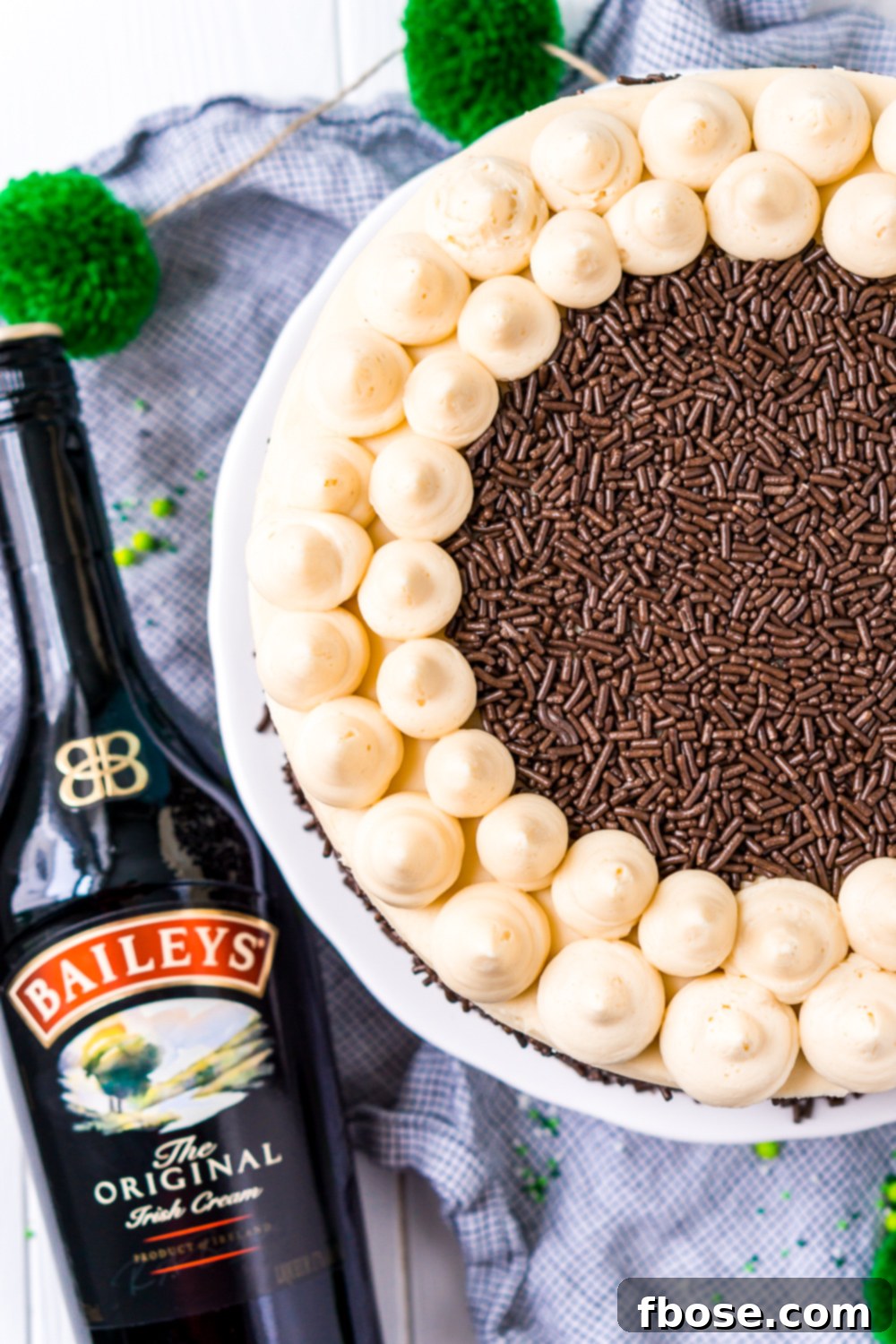 Overhead shot of a beautifully frosted Chocolate Guinness Cake with a bottle of Irish Cream Liqueur and a bottle of Guinness stout in the background, highlighting the key ingredients.