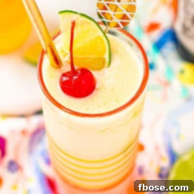 Close up photo of a pineapple daiquiri garnished with a maraschino cherry, lime wedge, and gold straw.