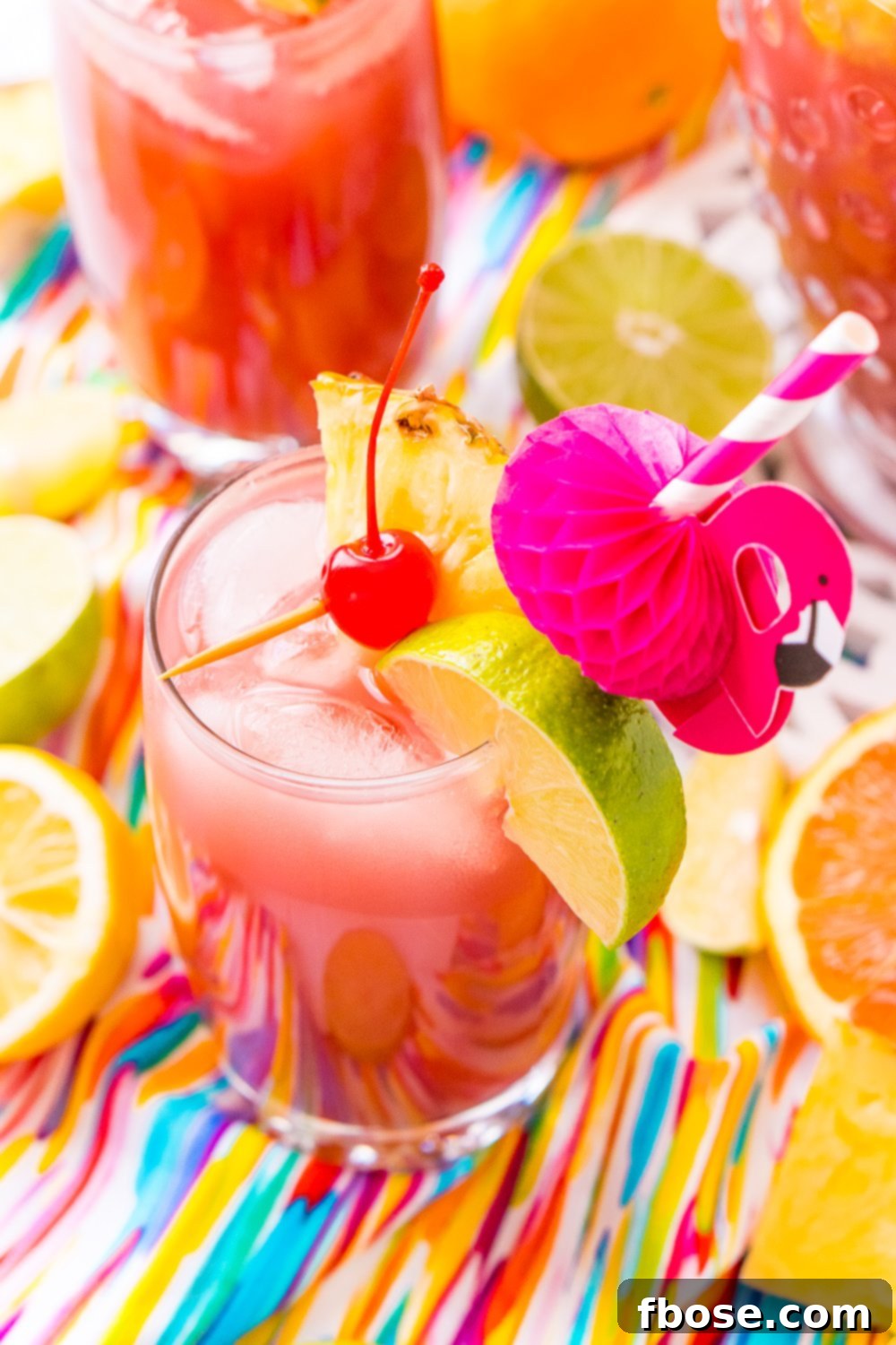 A beautiful glass of Rum Punch with fresh pineapple, cherry, and lime garnishes, evoking Caribbean vacation vibes. This large batch cocktail is ideal for summer parties, blending orange, pineapple, cranberry, lime, and lemon juices with ginger ale and three types of rum.