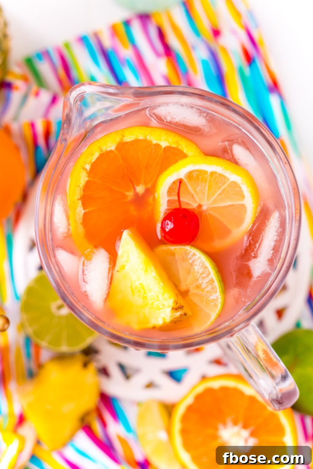 A pitcher of Caribbean-inspired Rum Punch sits on a colorful napkin, surrounded by fresh fruit slices, ready to be poured and enjoyed.