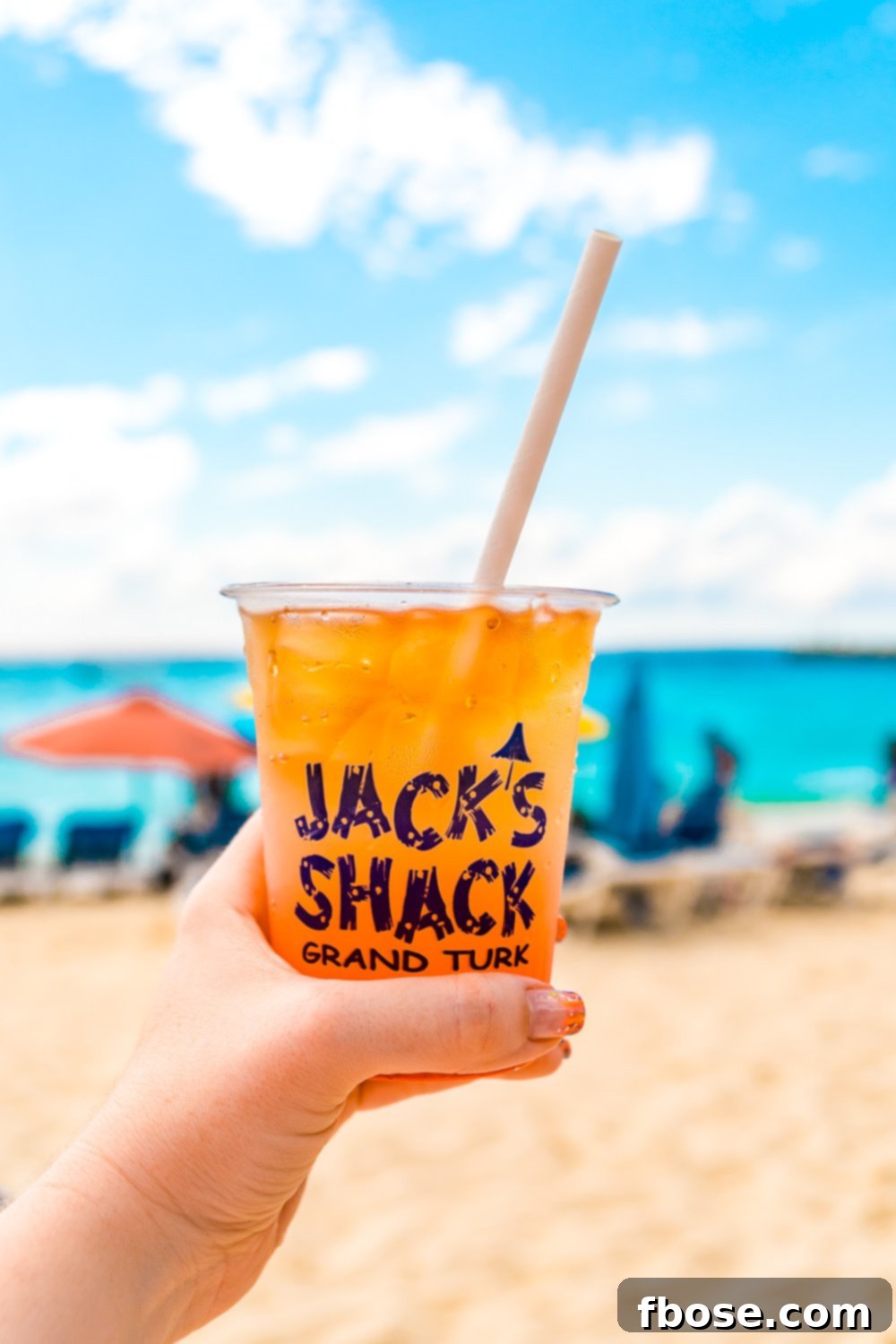 A close-up of a glass of Jack's Shack Rum Punch on Grand Turk, with the ocean in the background, symbolizing the authentic island experience that inspired this recipe.