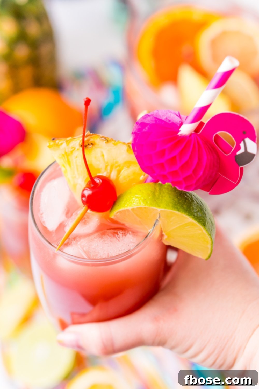 A woman's hand holding a glass of Caribbean Rum Punch, garnished with a cherry, lime wedge, and pineapple wedge, served with a playful flamingo paper straw, capturing the essence of a tropical summer drink.