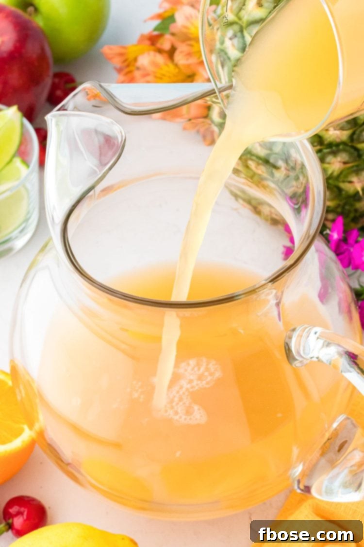 Orange, pineapple, guava juice being poured into a glass pitcher.