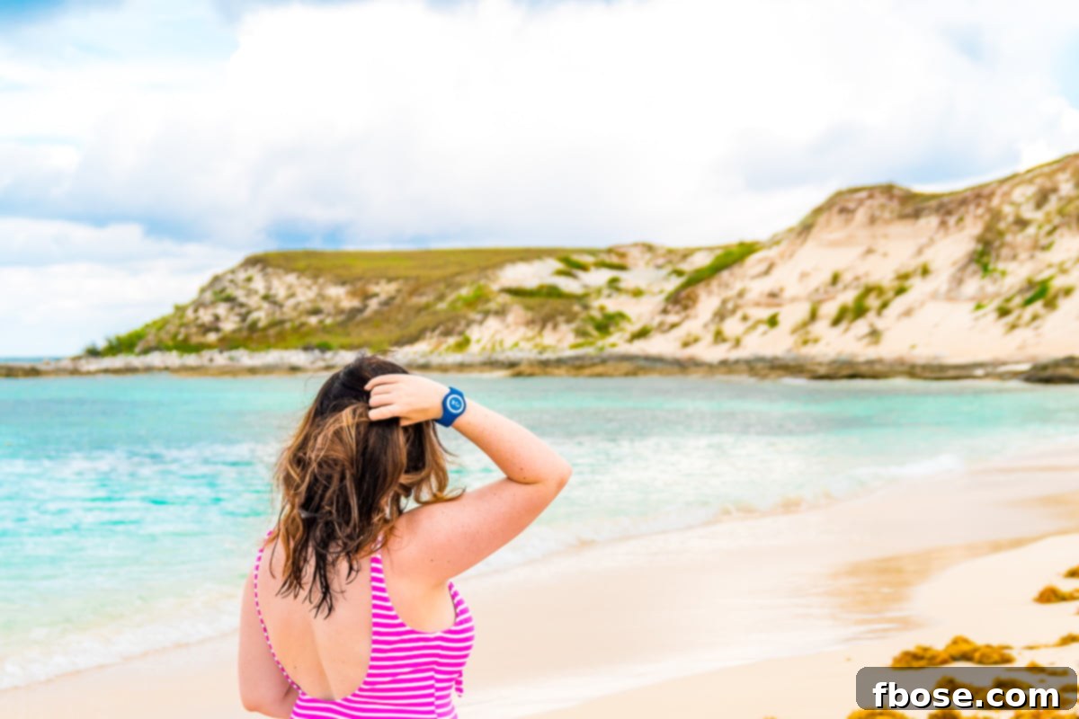 Grand Turk Island: Your Port Adventure Guide 11 A woman stands with her back to the camera on a pristine beach, dressed in a pink swimsuit with a hand casually in her hair, enjoying the serene ocean view.