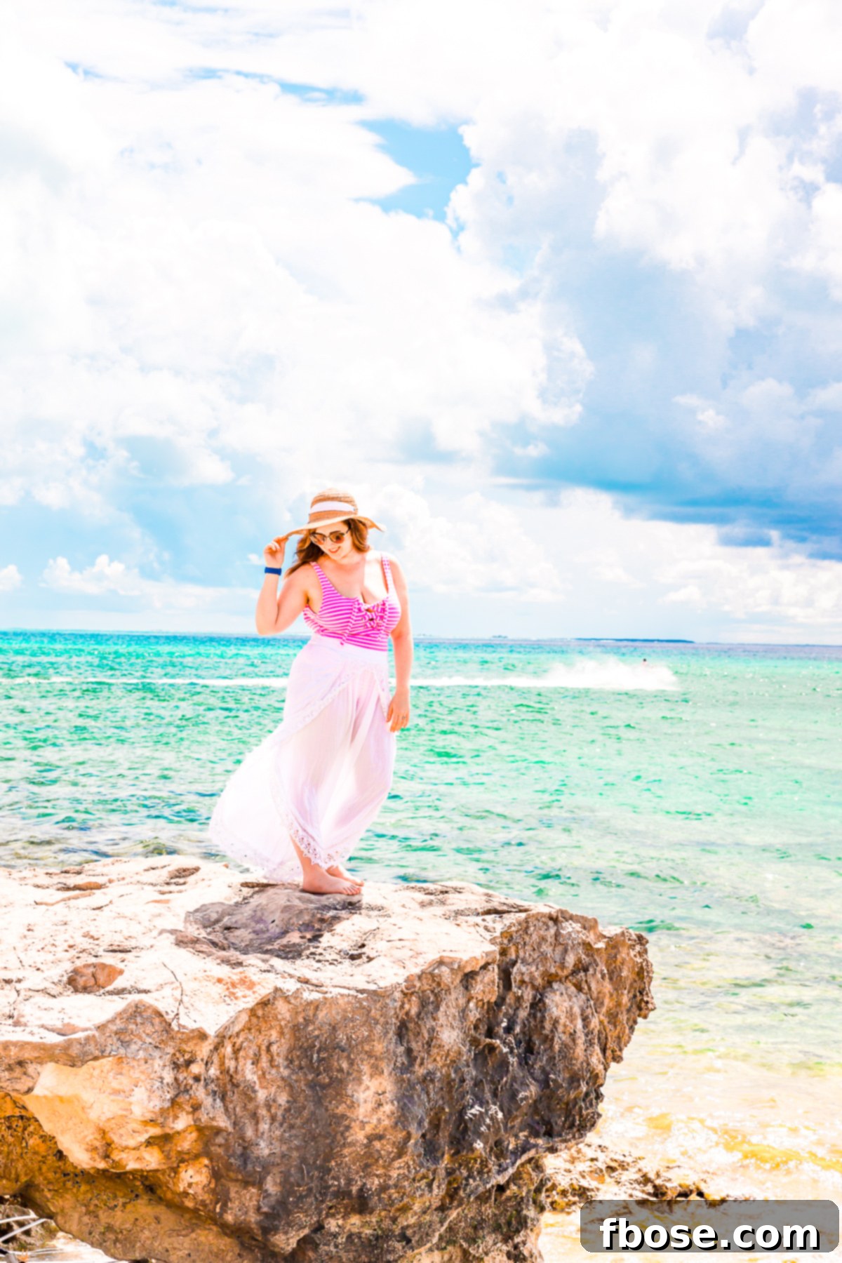 Grand Turk Island: Your Port Adventure Guide 12 A woman stands atop a small cliff, gazing out at the mesmerizing turquoise waters of the Grand Turk Cruise Port. The vibrant blues of the sea meet the distant horizon, creating a picturesque scene.