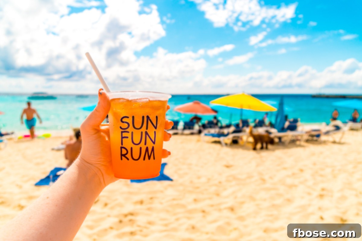 Grand Turk Island: Your Port Adventure Guide 14 A woman's hand holds a vibrant cup of rum punch, set against the backdrop of a sunny beach dotted with inviting beach umbrellas, capturing the essence of a relaxed Caribbean getaway.