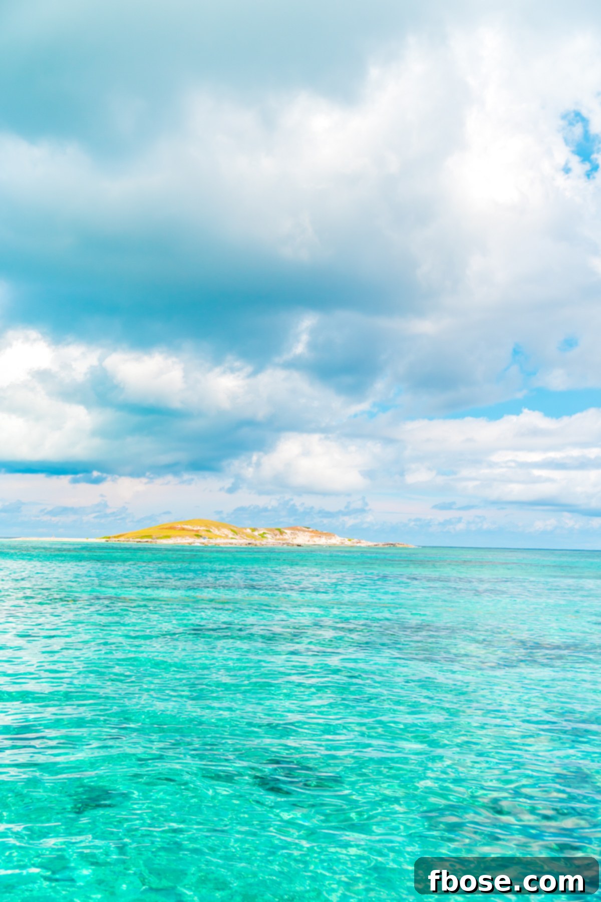 Grand Turk Island: Your Port Adventure Guide 5 An idyllic Caribbean island, bathed in brilliant blue skies, is surrounded by an expanse of clear, azure water. This aerial view captures the serene and inviting beauty of the island paradise.