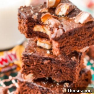 Close up photo of a stack of three Twix Caramel Brownies with a bite taken out of the top brownie.
