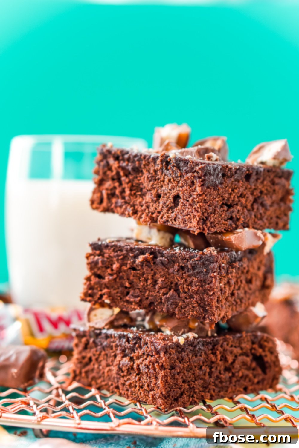 Twix Caramel Fudge Brownies 4 Stack of three Twix Caramel Brownies on a copper cooling rack with a glass of milk in the background.