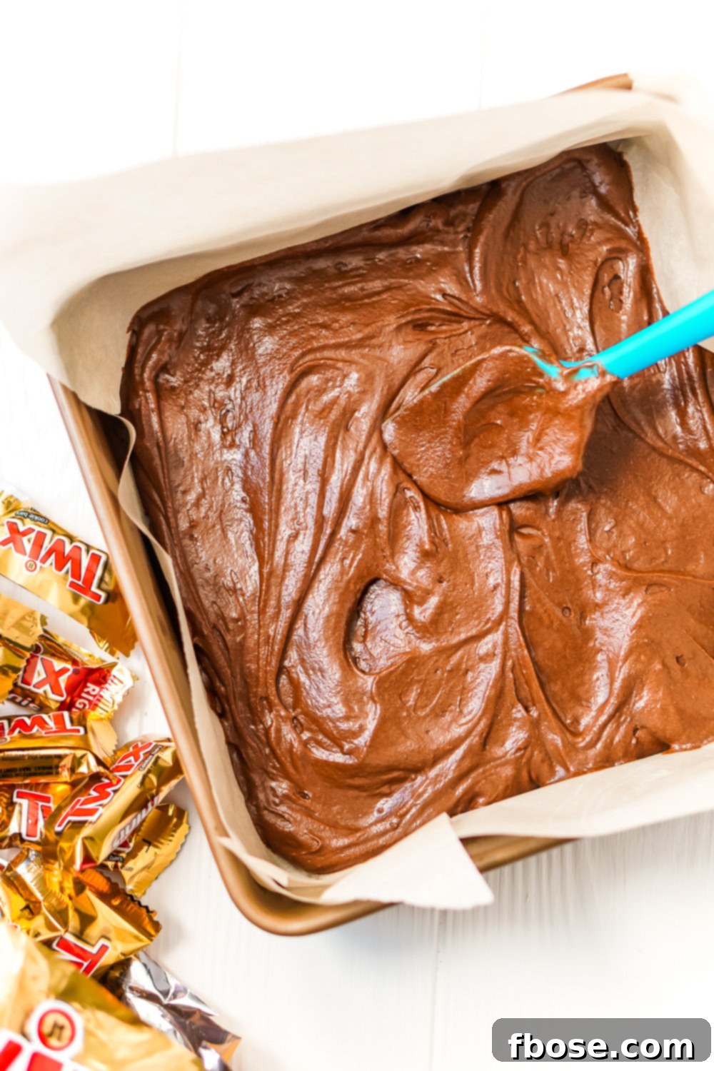 Twix Caramel Fudge Brownies 7 Brownie batter being spread in a baking dish with a rubber spatula.