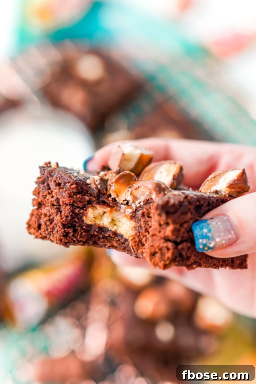 Twix Caramel Fudge Brownies 8 Woman's hand holding a Twix Caramel Brownie with a bite taken out of it.