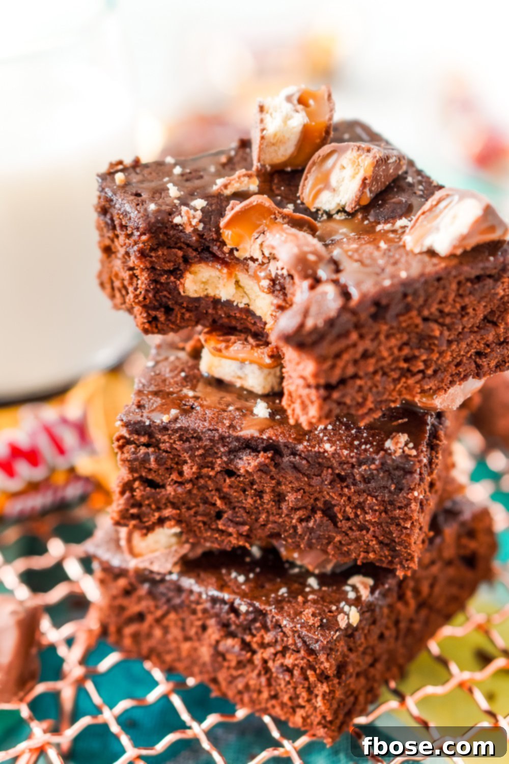 Twix Caramel Fudge Brownies 10 Close up photo of a stack of three Twix Caramel Brownies with a bite taken out of the top brownie.