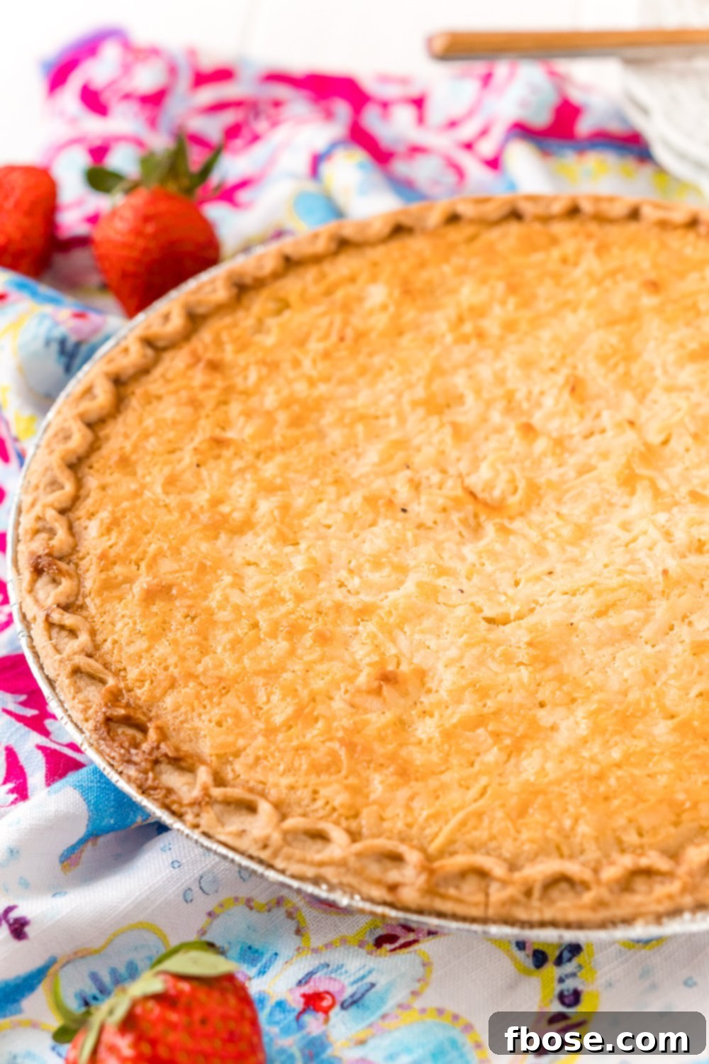 Photo of a Coconut Custard Pie in a pie tin with strawberries scattered around.