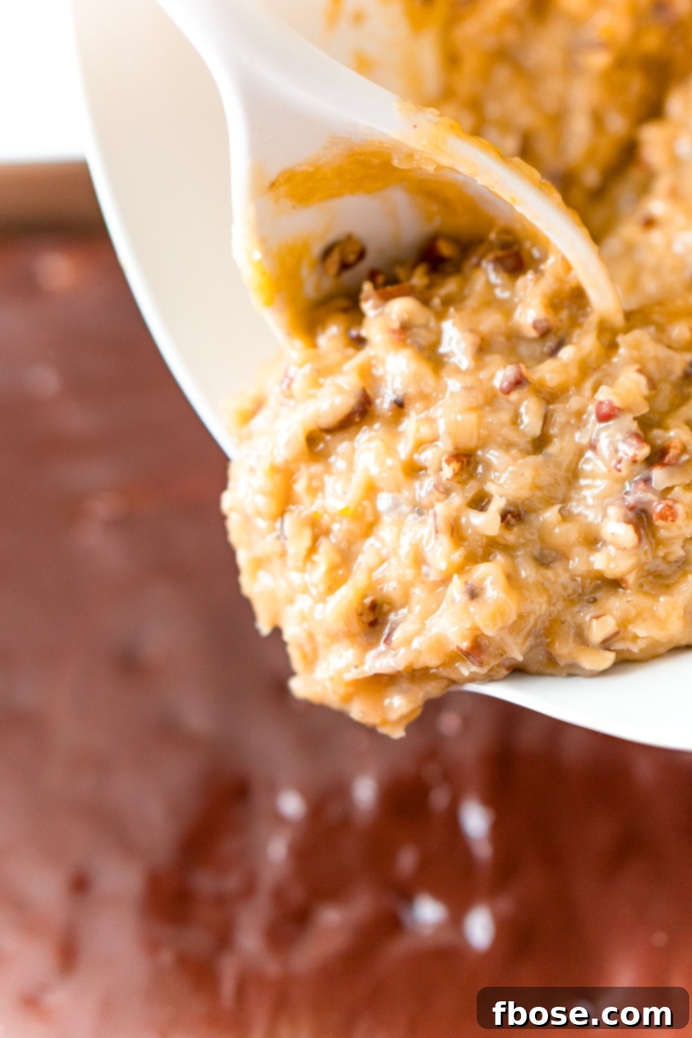 Coconut Pecan Frosting being poured onto a chocolate cake.