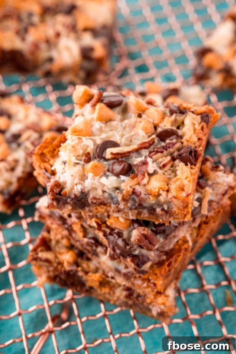 Seven-Layer Magic Bars 2 Close up photo of golden brown Hello Dolly Bars, freshly baked and stacked on a copper wire rack, showcasing their irresistible layers of chocolate, butterscotch, pecans, and coconut.
