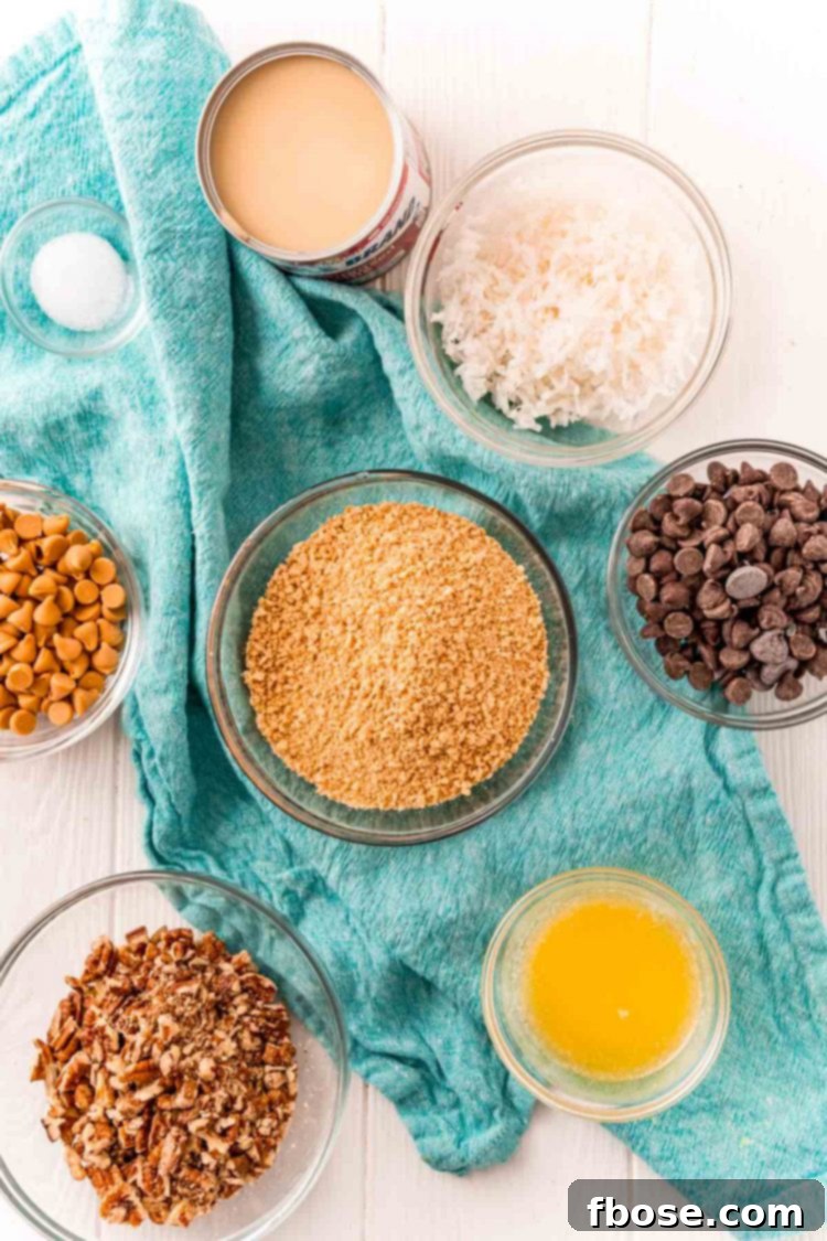 Seven-Layer Magic Bars 4 Ingredients laid out on a white table with a blue napkin, ready to make Hello Dolly or 7 Layer Bars, featuring graham crackers, chips, pecans, coconut, butter, and condensed milk.