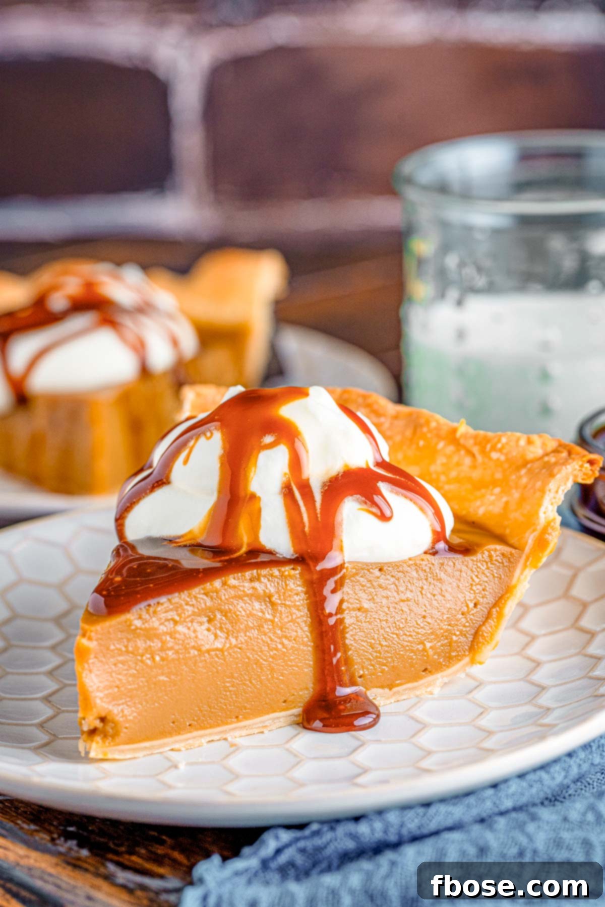 Close up photo of a slice of butterscotch pie on a white plate on a blue napkin.