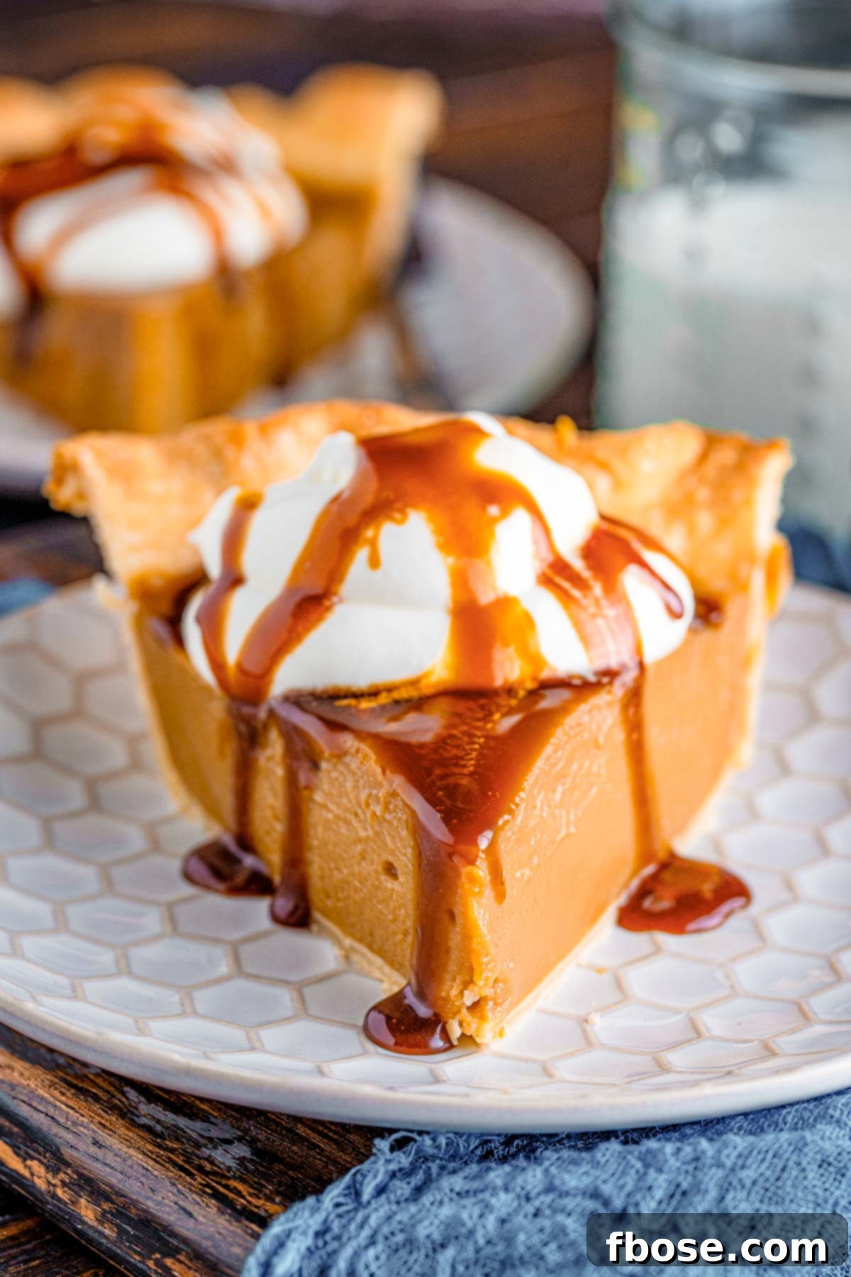 Close up photo of a slice of butterscotch pie on a white plate on a blue napkin.