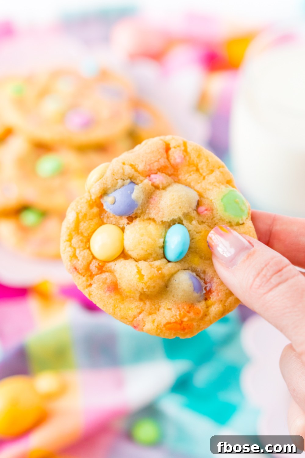 A woman's hand gently holding a freshly baked Easter M&M cake mix cookie, highlighting its appeal.