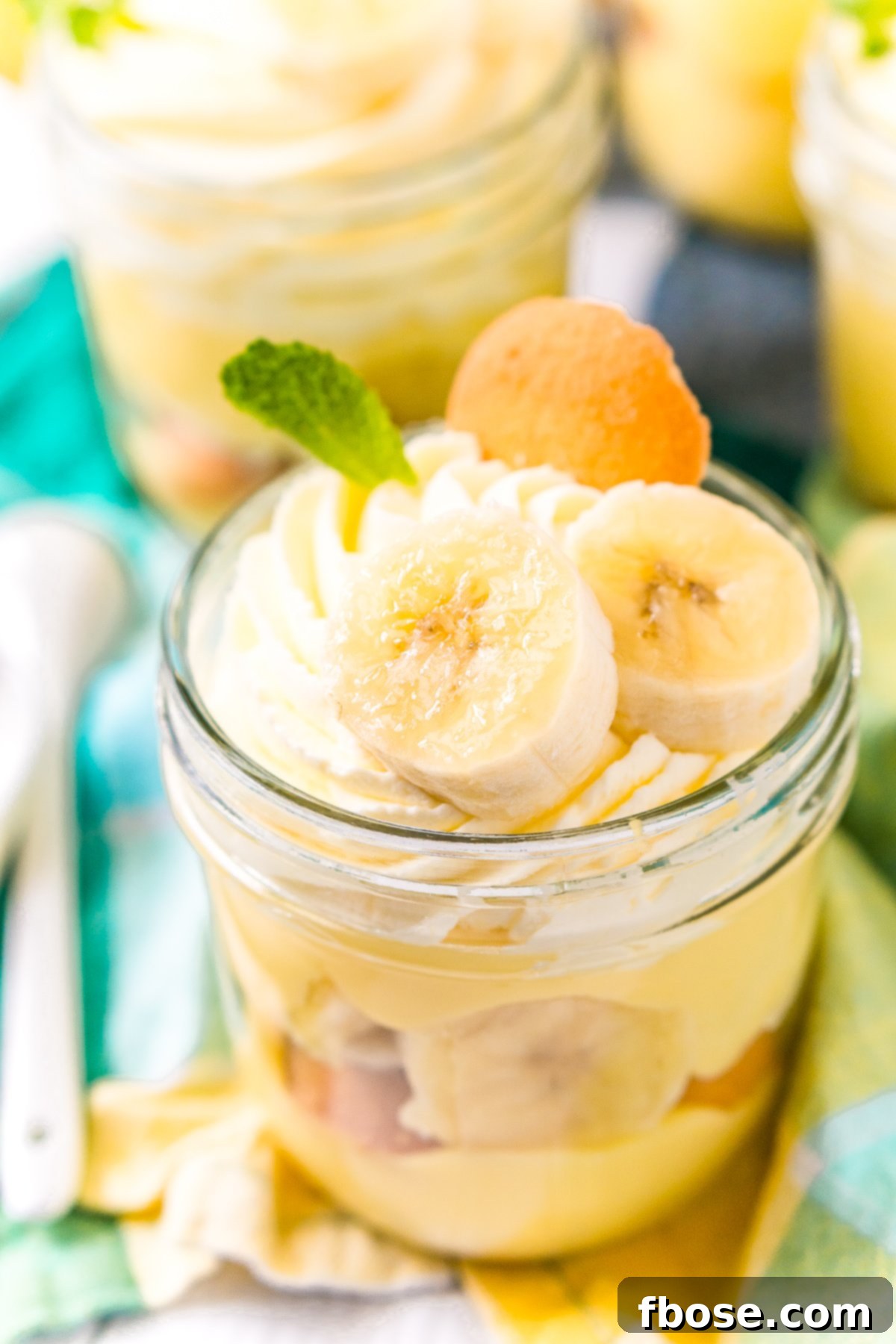 Small jar filled with banana pudding with banana slices, mint leaf, and nilla wafer on top.