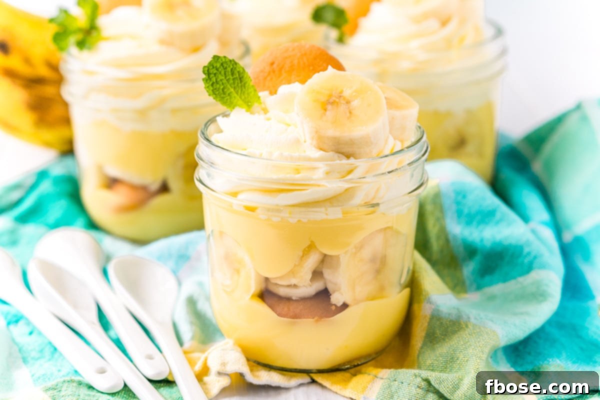 Three mason jars filled with banana pudding on a blue napkin with white spoons to the side.