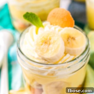 Small jar filled with banana pudding with banana slices, mint leaf, and nilla wafer on top.