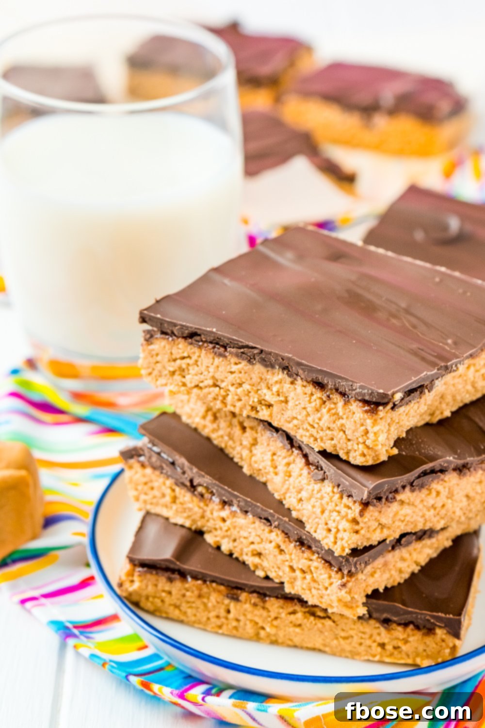 Chocolate Peanut Butter Bars on white plate with blue trim on a coloful napkin next to a glass of milk.