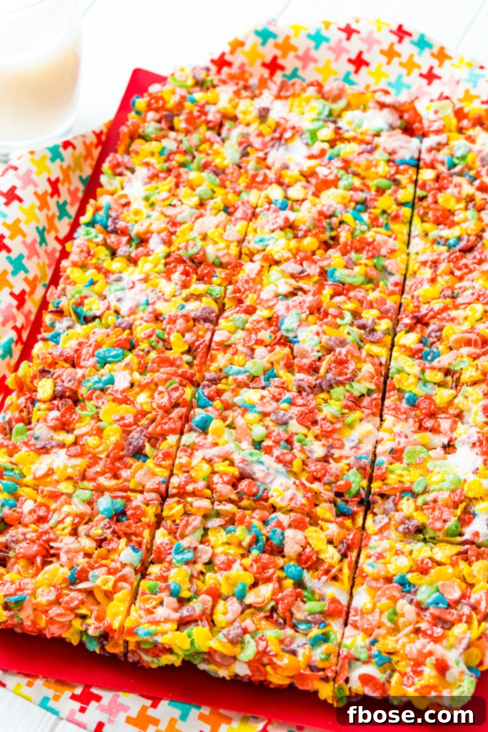 A sheet of colorful Fruity Pebbles Treats, neatly cut into squares but still arranged together on a red cutting board. The vibrant colors of the cereal stand out against the soft, chewy marshmallow base.