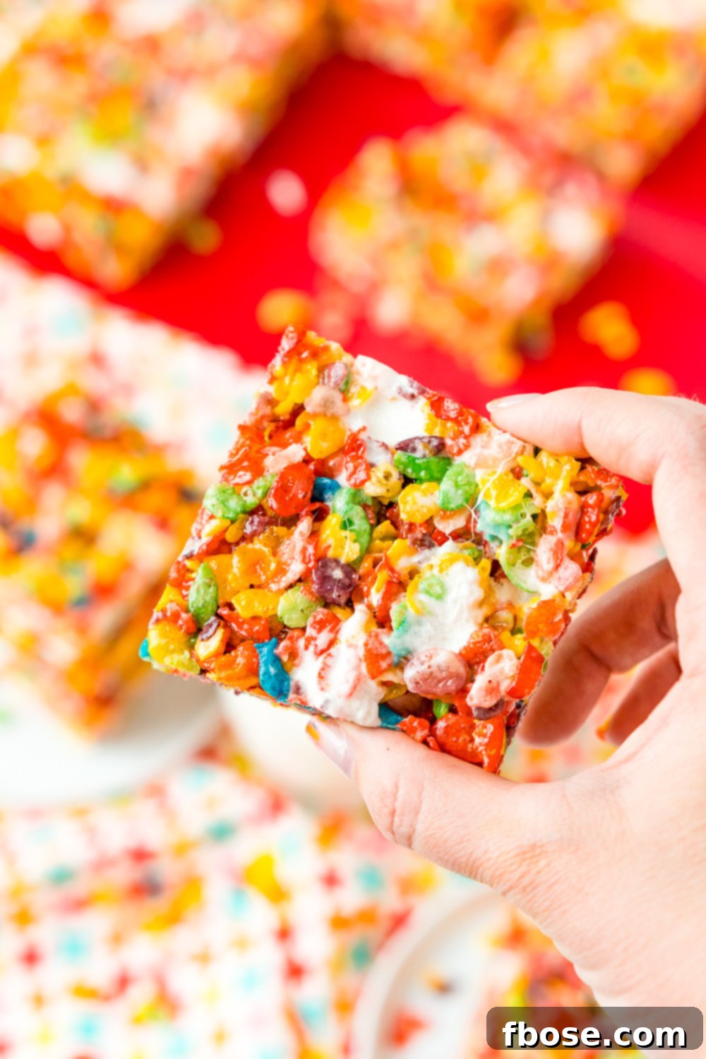A woman's hand reaches for a Fruity Pebbles Treat, with more colorful treats visible on a red cutting board in the background. The scene suggests an irresistible snack moment.