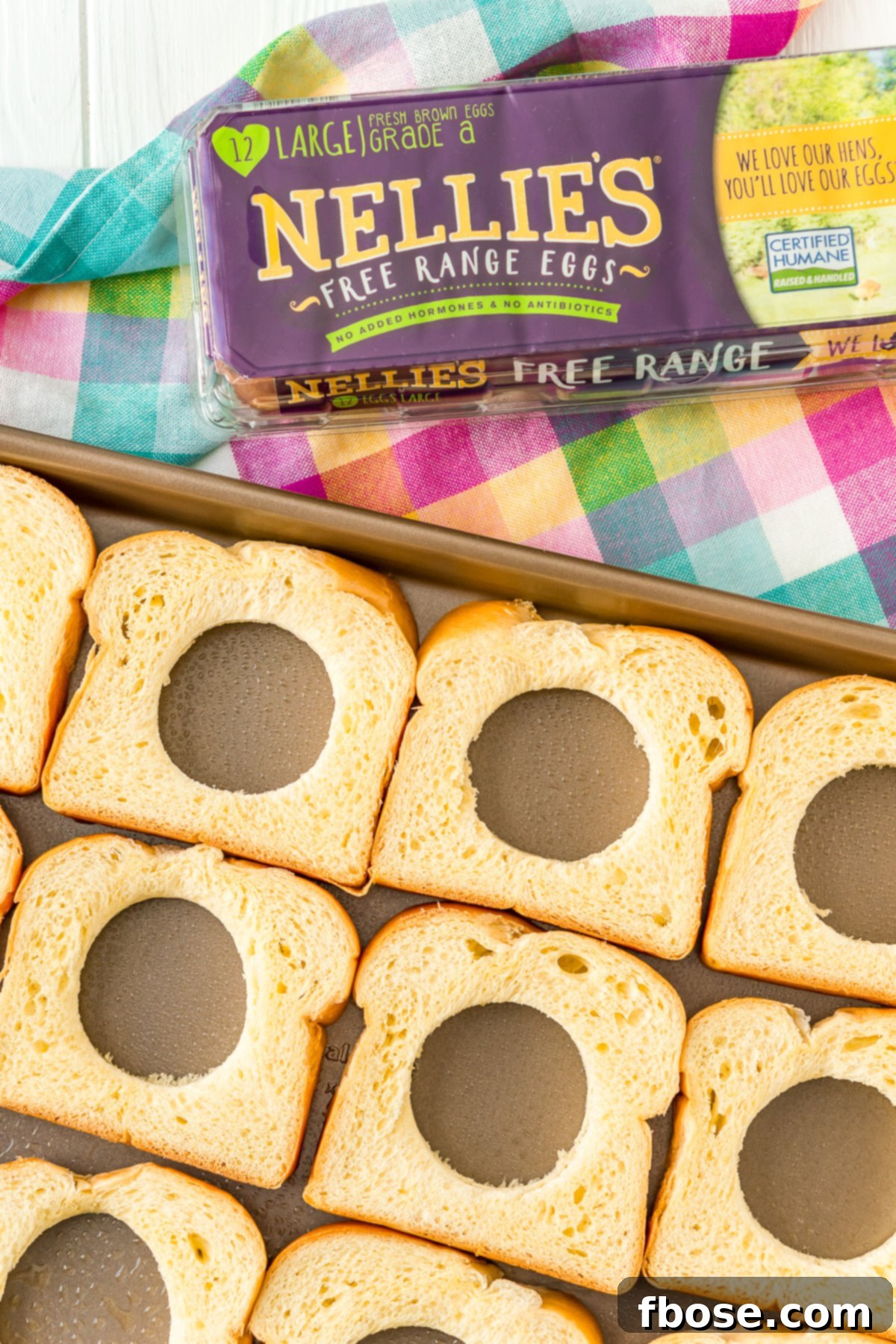 Bread slices with holes cut out, arranged on a sheet pan, ready for eggs.