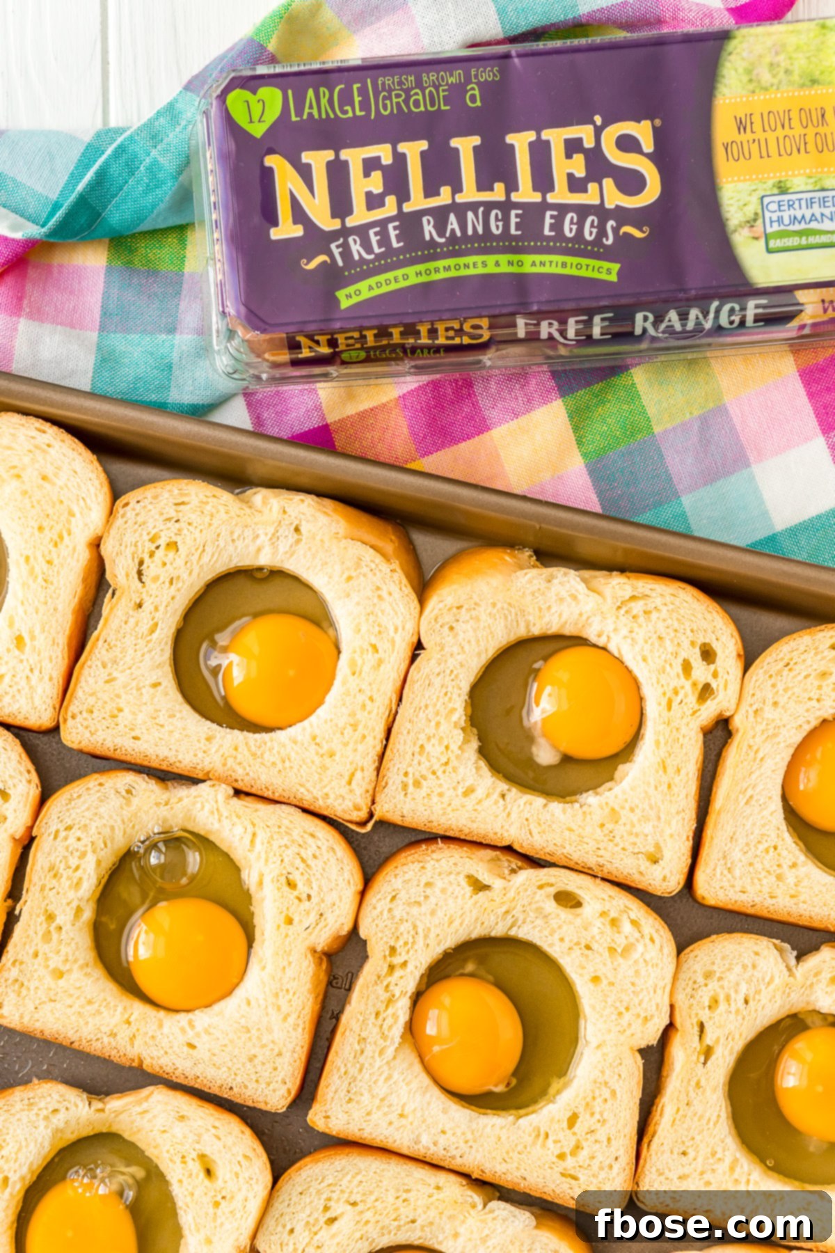 Eggs cracked into the holes of bread on a sheet pan, ready for baking.